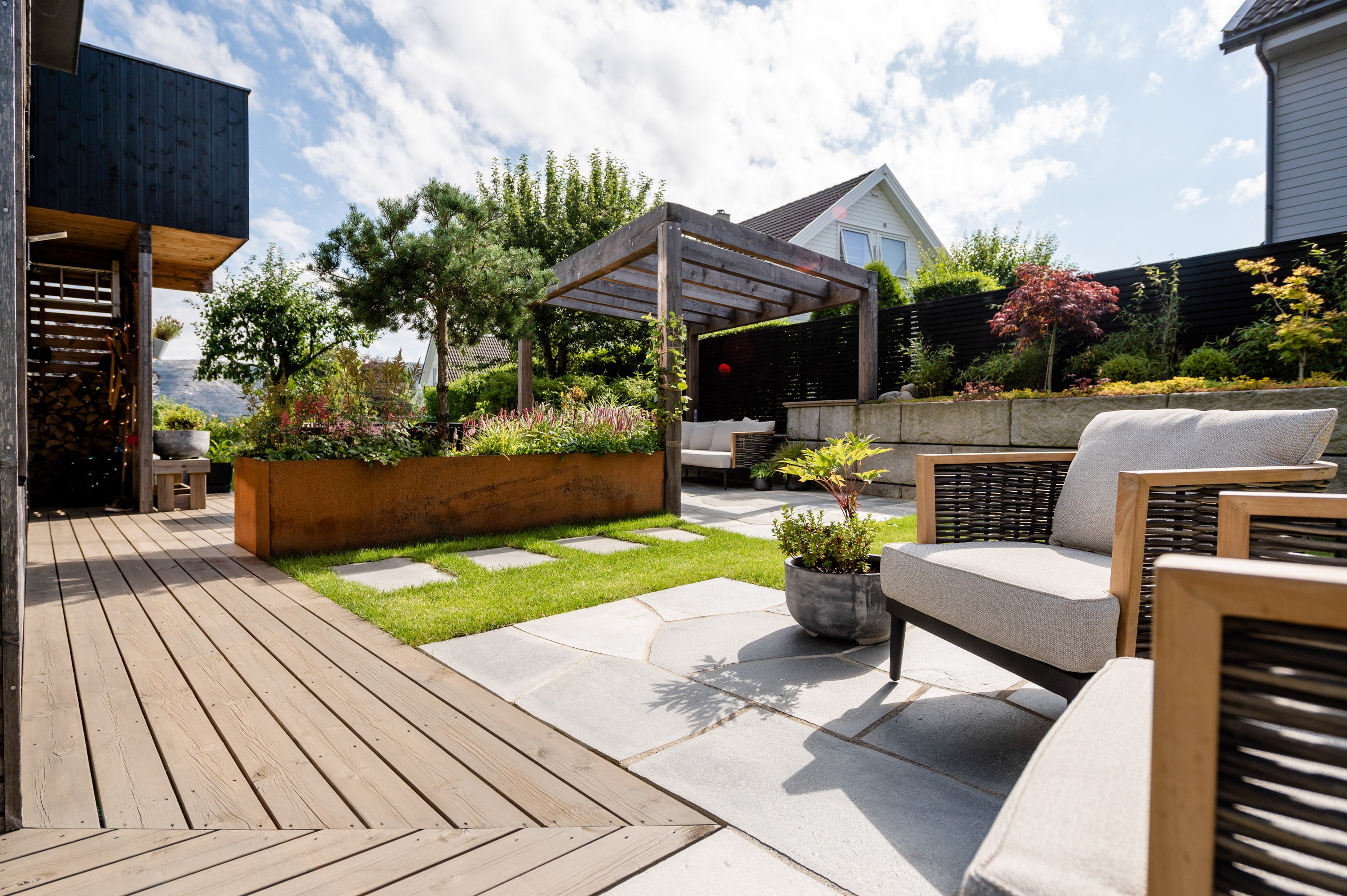 Lys Oppdal tråkkheller lagt i plen og skiferdekke, med terrassebord, pergola og loungemøbler i solrik hage
